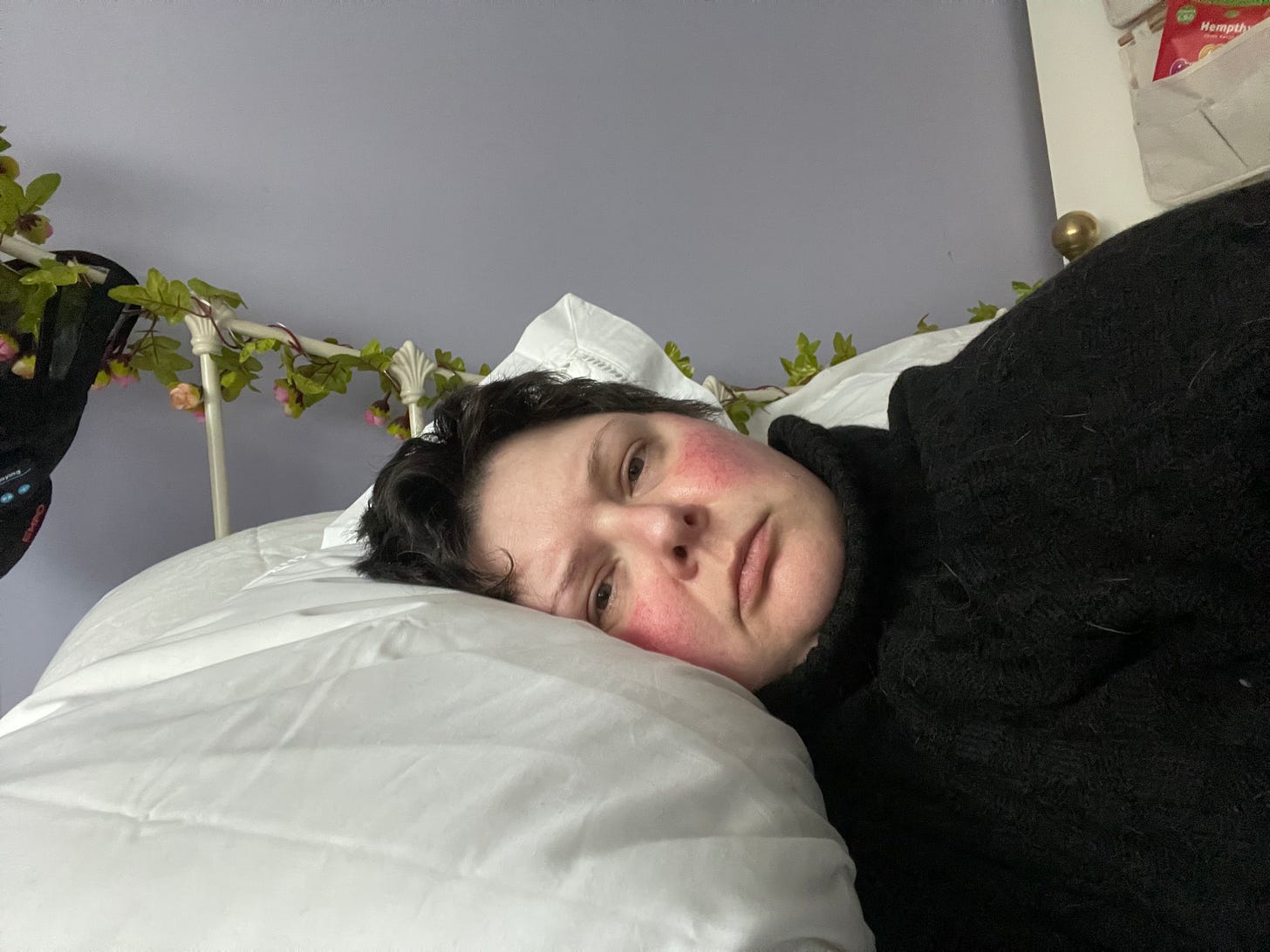Cass lies in bed, only her face and shoulders visible, looking straight into the camera. Cass lies in bed, only her face and shoulders visible, looking straight into the camera.