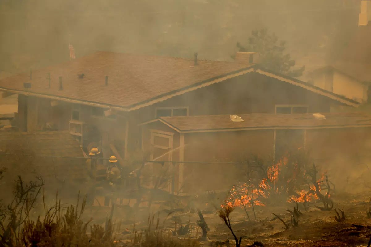 Firefighters standing in the defensible space around another home while fighting an active fire; the home itself has not caught fire Firefighters standing in the defensible space around another home while fighting an active fire; the home itself has not caught fire