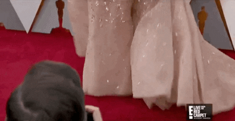 A woman in a pink flowing gown walks the Oscars red carpet.