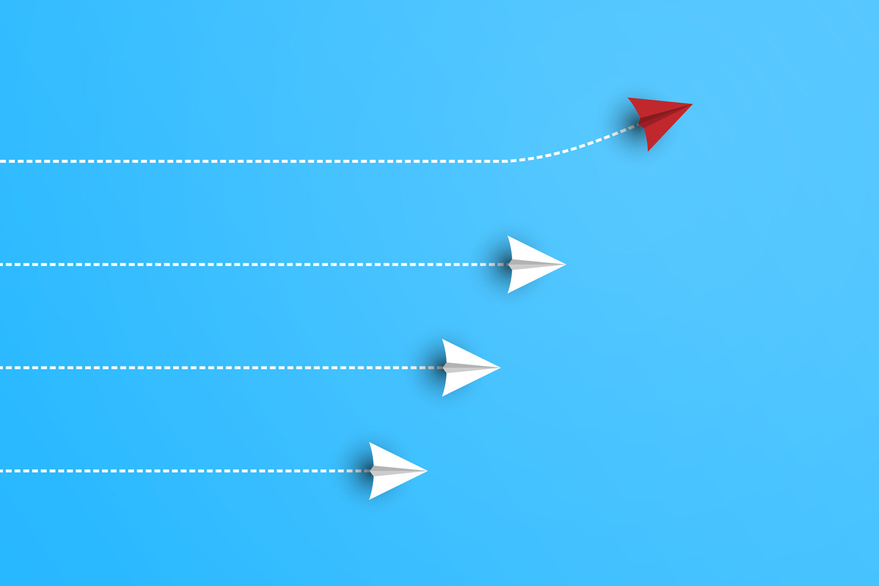 A single paper airplane diverges from the crowd.