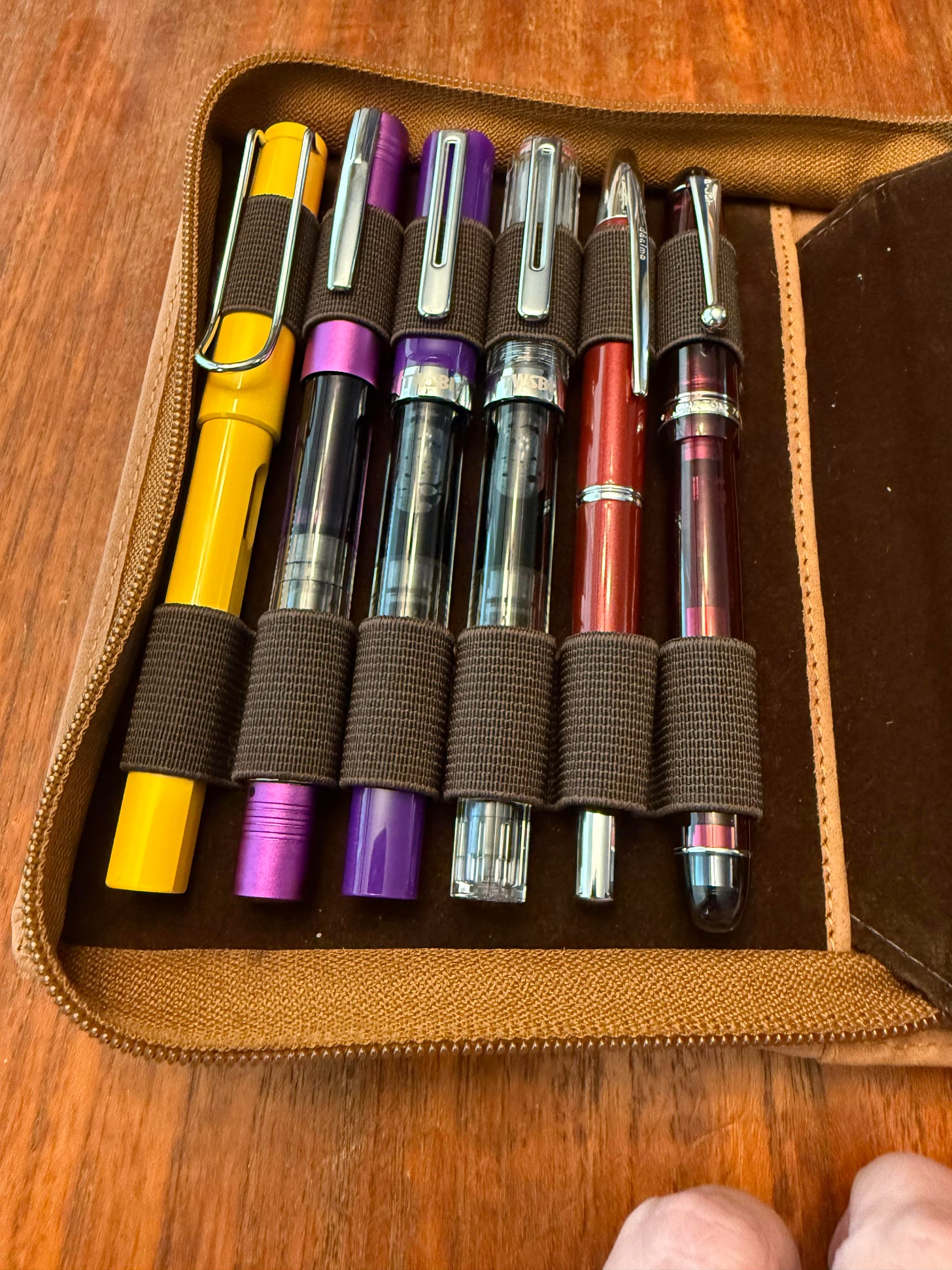 six fountain pens inside a brown leather pen case