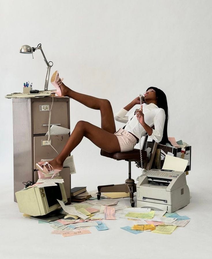 This may contain: a woman sitting in an office chair with her feet up on a desk full of papers