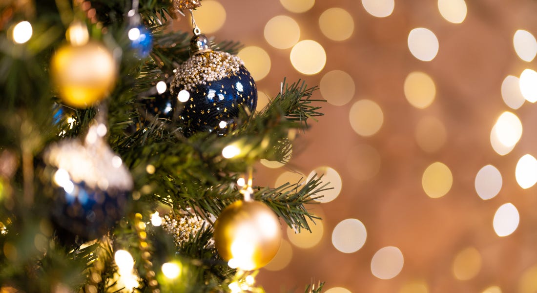 A close-up shot of a Christmas tree with dark blue and gold baubles with twinkly lights behind it