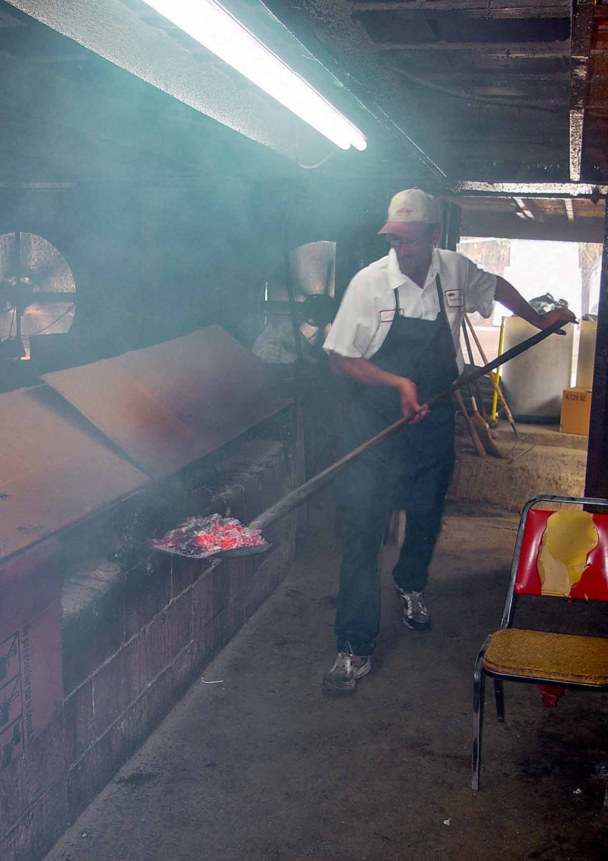 Ricky Parker shoveling hot coals into his barbecue smoker Ricky Parker shoveling hot coals into his barbecue smoker