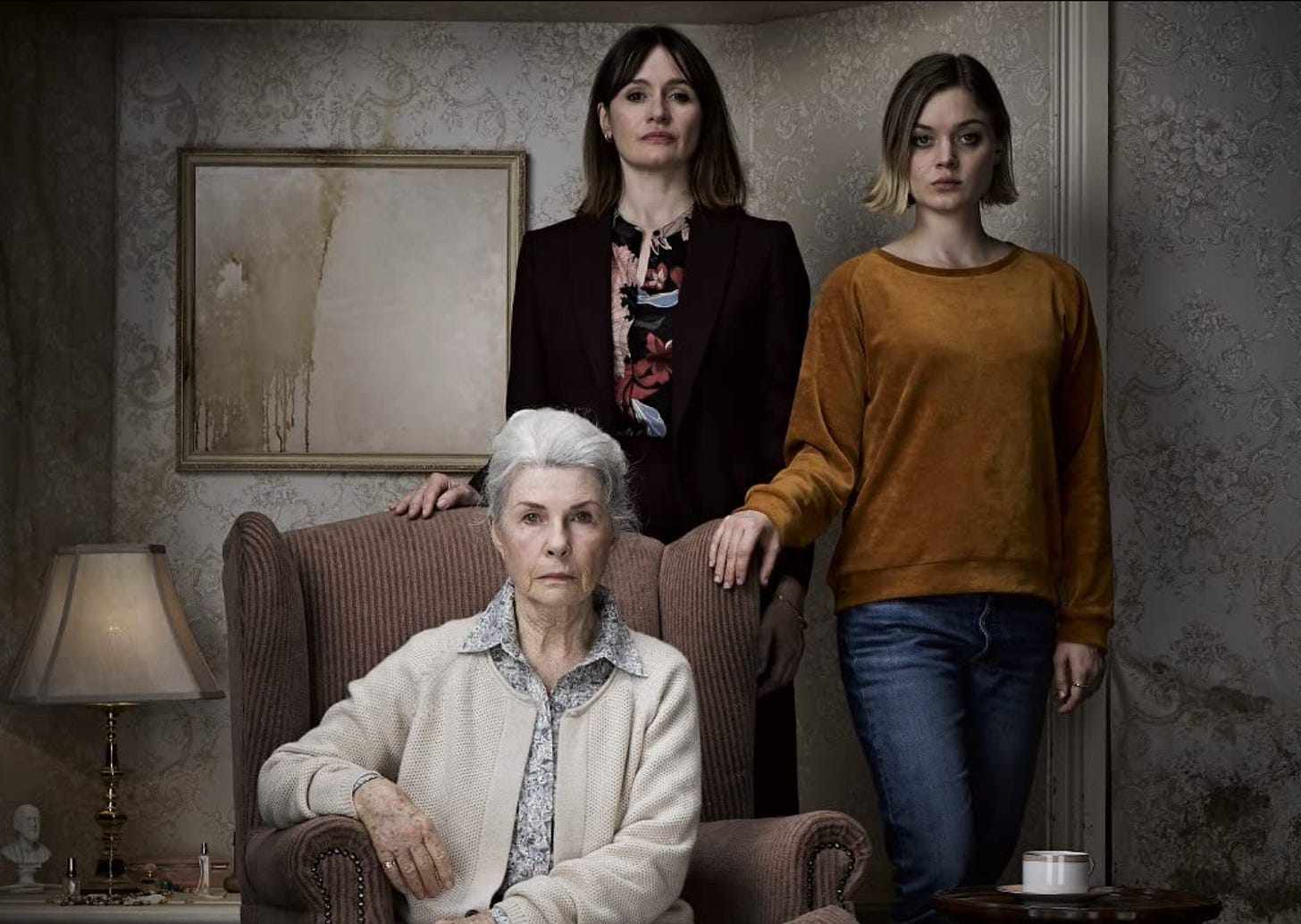Two women are standing next to a woman seated in an arm chair.