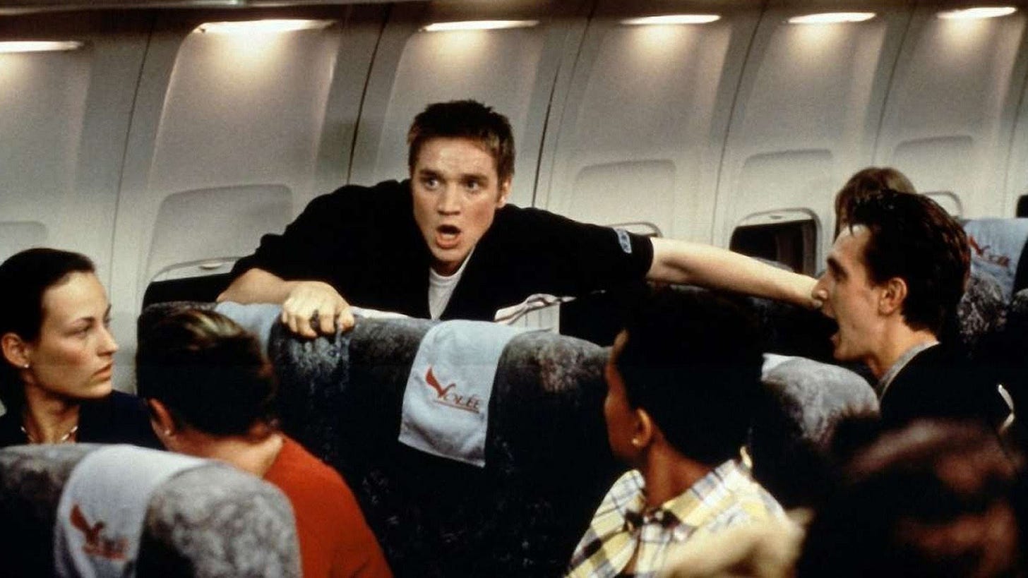 Devon Sawa looking freaked out on a plane while on the passengers stare at him, confused