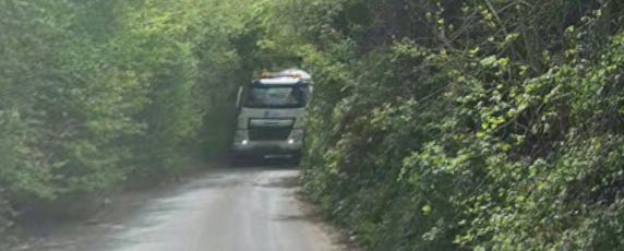 A rural country single lane with a cement lorry coming through. The verges have been eaten away and crumbling severely. Mock Lane, Singleton/Chilmington Kent
