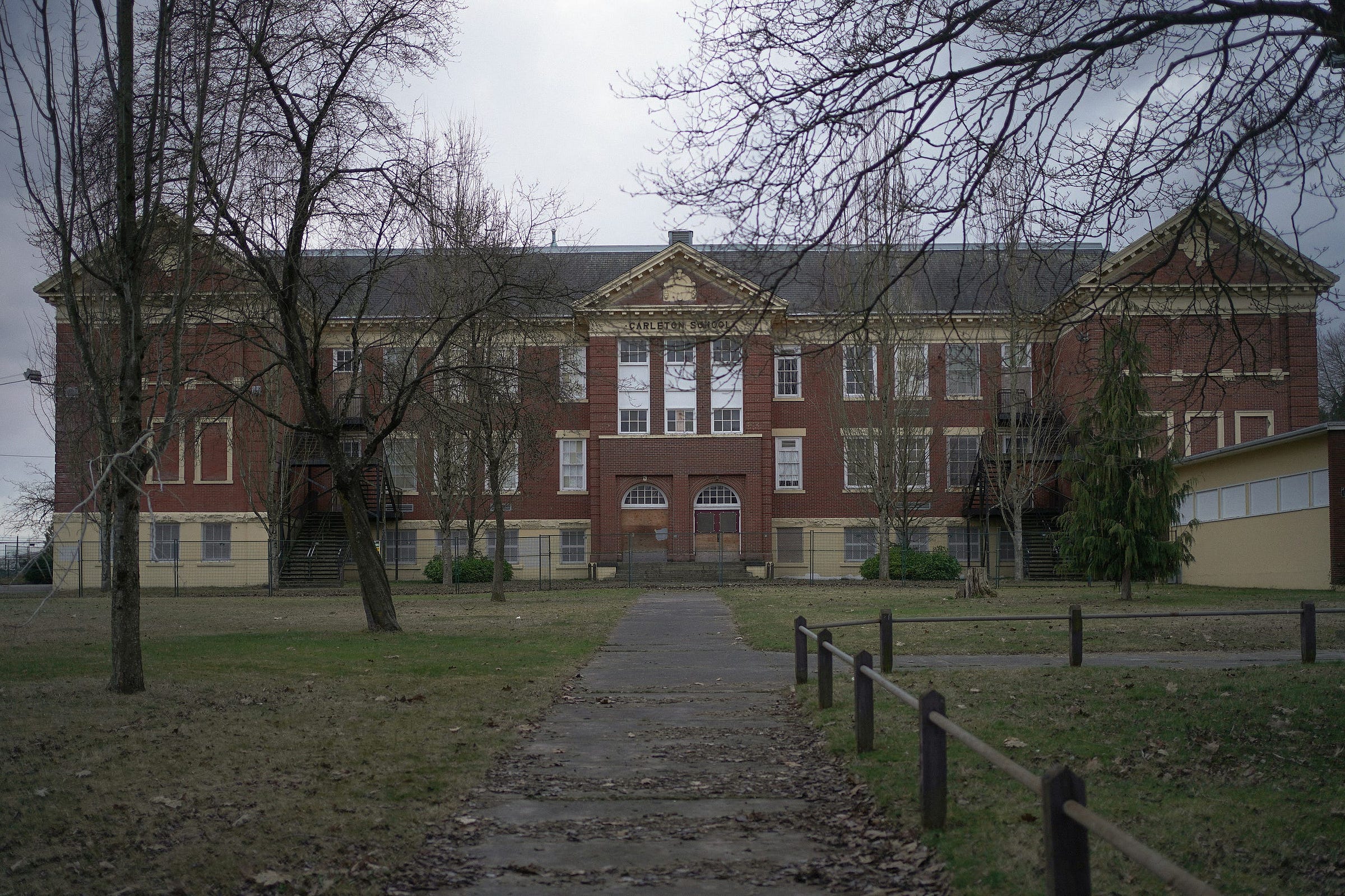 An old brick school with a front yard on a cloudy day with leafless trees in autumn or winter. An old brick school with a front yard on a cloudy day with leafless trees in autumn or winter.