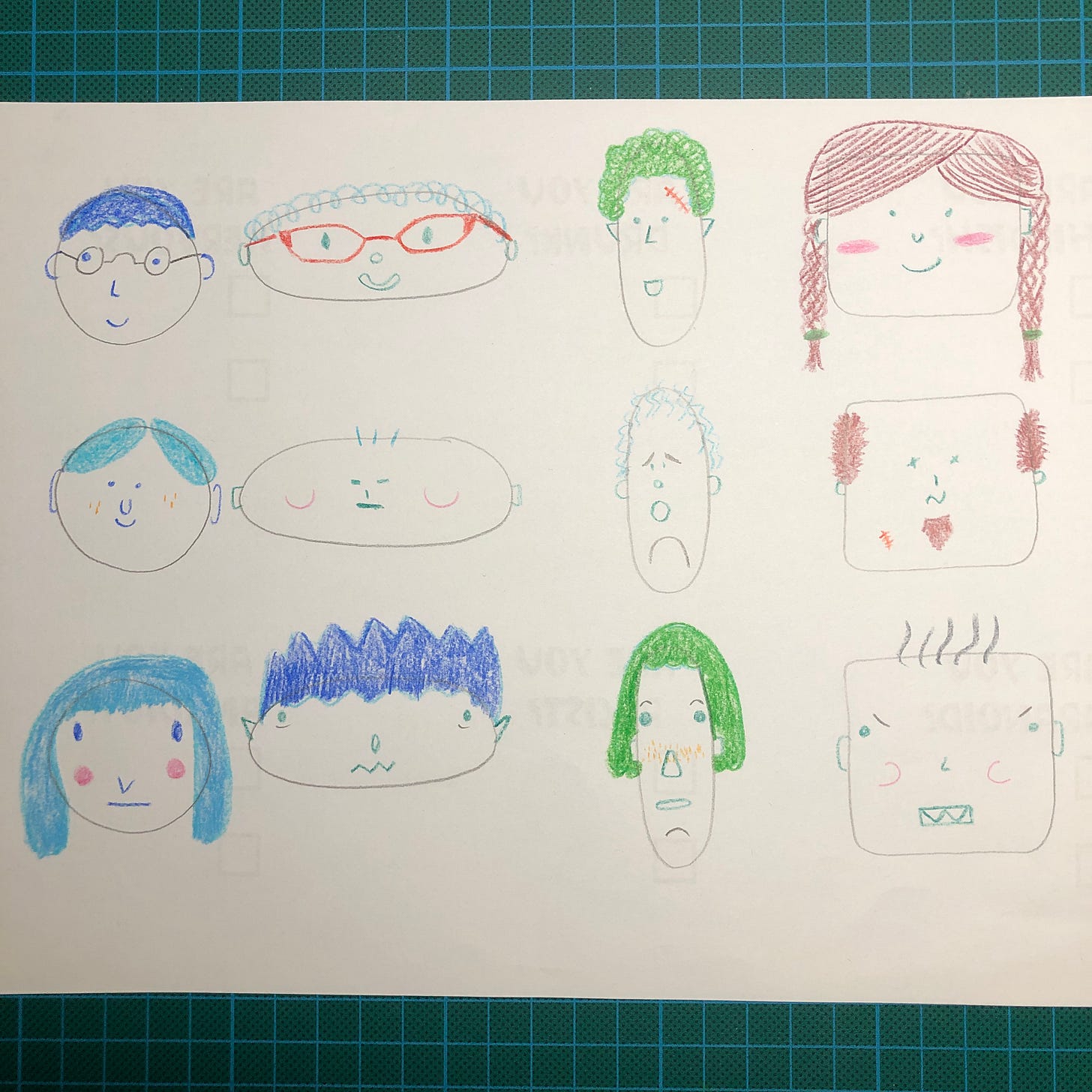 Photo d'une feuille de papier blanc où j'ai dessiné au crayon graphite et crayons de couleurs, 12 têtes de personnages avec des caractéristiques simplifiées en quelques formes.