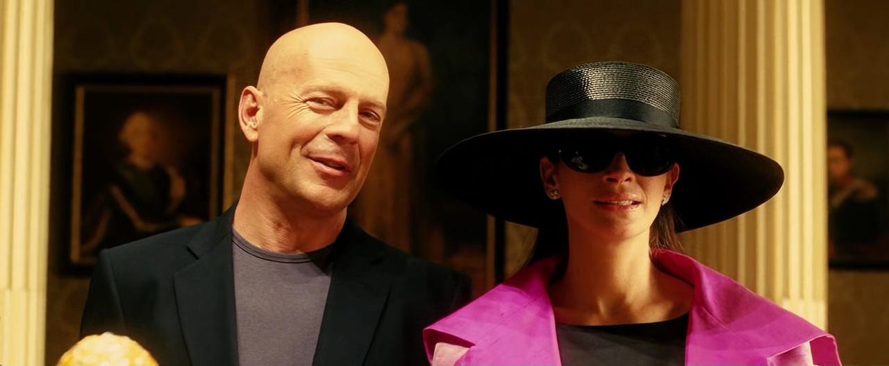 Still of Bruce Willis and Julia Roberts in Ocean's Twelve. They're standing side by side, looking at the camera. Julia is technically Tess Ocean pretending to be Julia Roberts, so she's wearing a hat and sunglasses.