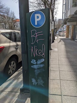 two signs with assorted and positive graffiti, including "BE NICE!" on a parking meter