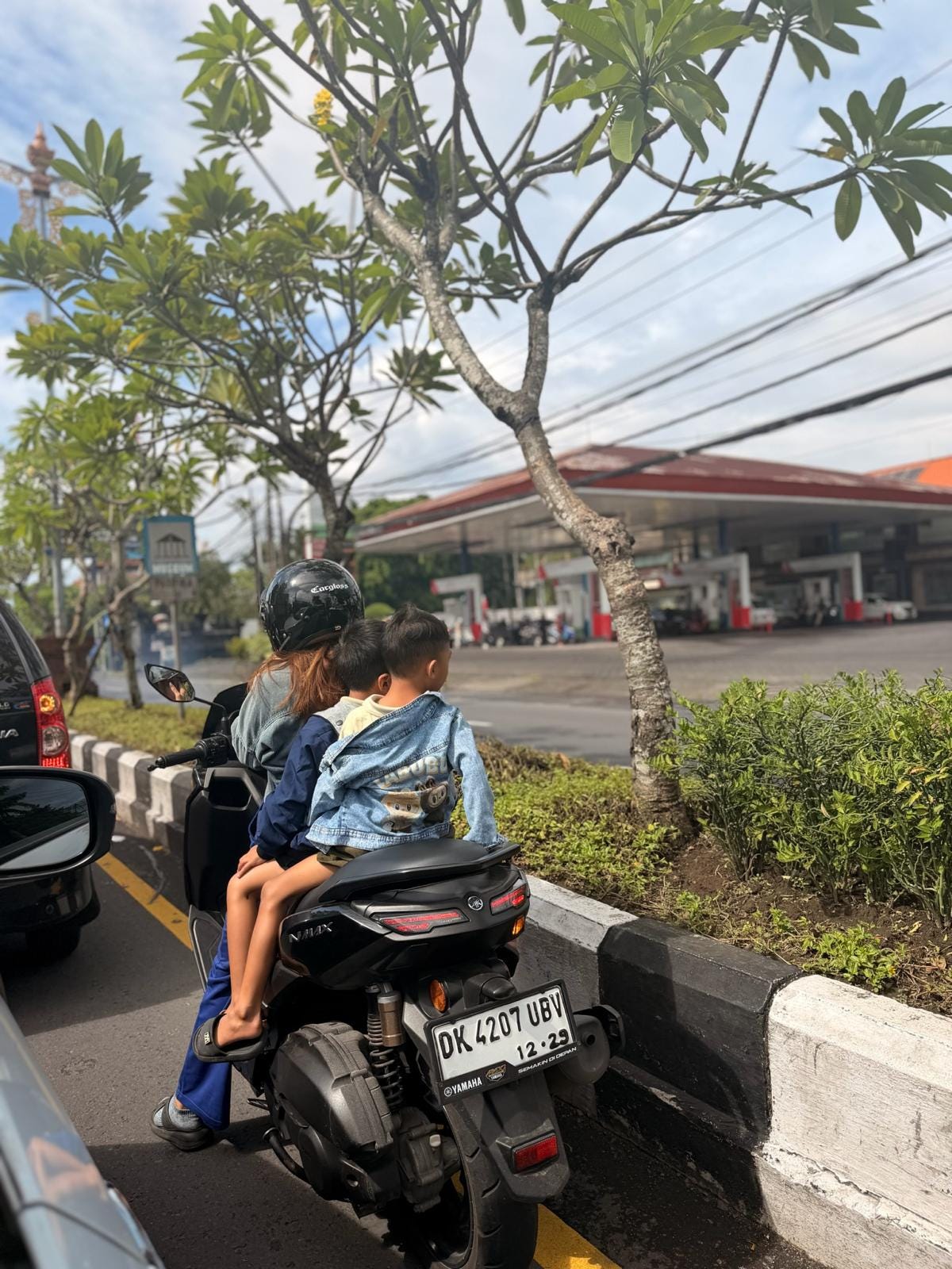 A family riding together on a motorbike in Bali during afternoon traffic.