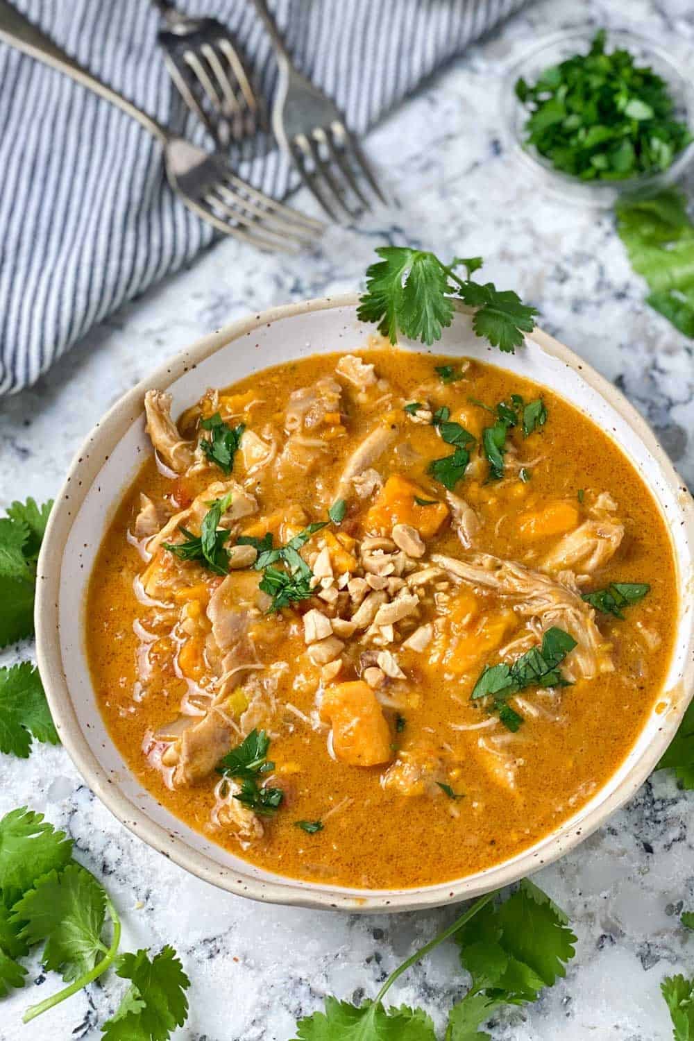 a white bowl filled with peanut chicken stew with sweet potatoes, garnished with chopped cilantro, 3 forks on the side a white bowl filled with peanut chicken stew with sweet potatoes, garnished with chopped cilantro, 3 forks on the side