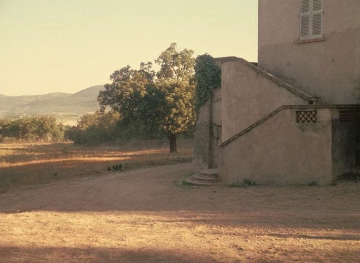 This may contain: an old building in the middle of a field with trees and hills in the background