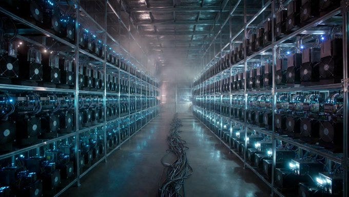 Rows of cryptocurrency mining rigs stretch into the distance inside a dimly lit industrial facility, with blue indicator lights glowing through haze and cables snaking across the floor, depicting large-scale Bitcoin mining operations Rows of cryptocurrency mining rigs stretch into the distance inside a dimly lit industrial facility, with blue indicator lights glowing through haze and cables snaking across the floor, depicting large-scale Bitcoin mining operations