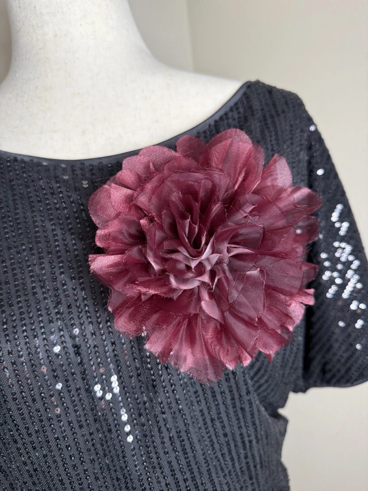 Burgundy organza flower brooch with layered petals and sequined accents on black top. Burgundy organza flower brooch with layered petals and sequined accents on black top.