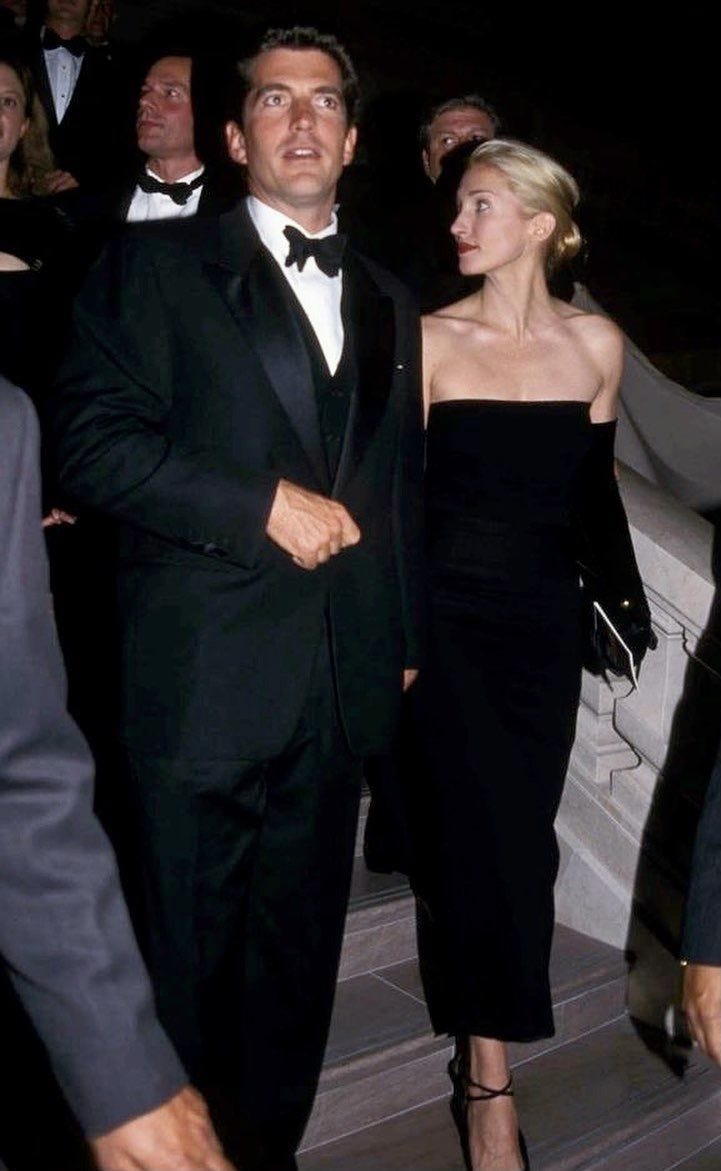 This may contain: a man in a tuxedo walking next to a woman wearing a black dress This may contain: a man in a tuxedo walking next to a woman wearing a black dress