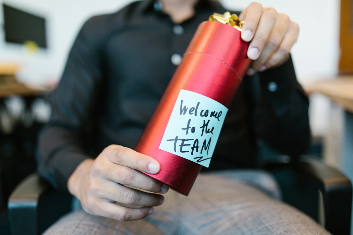 Free A red gift box held by a person with a welcome to the team note, ideal for new hire announcements. Stock Photo