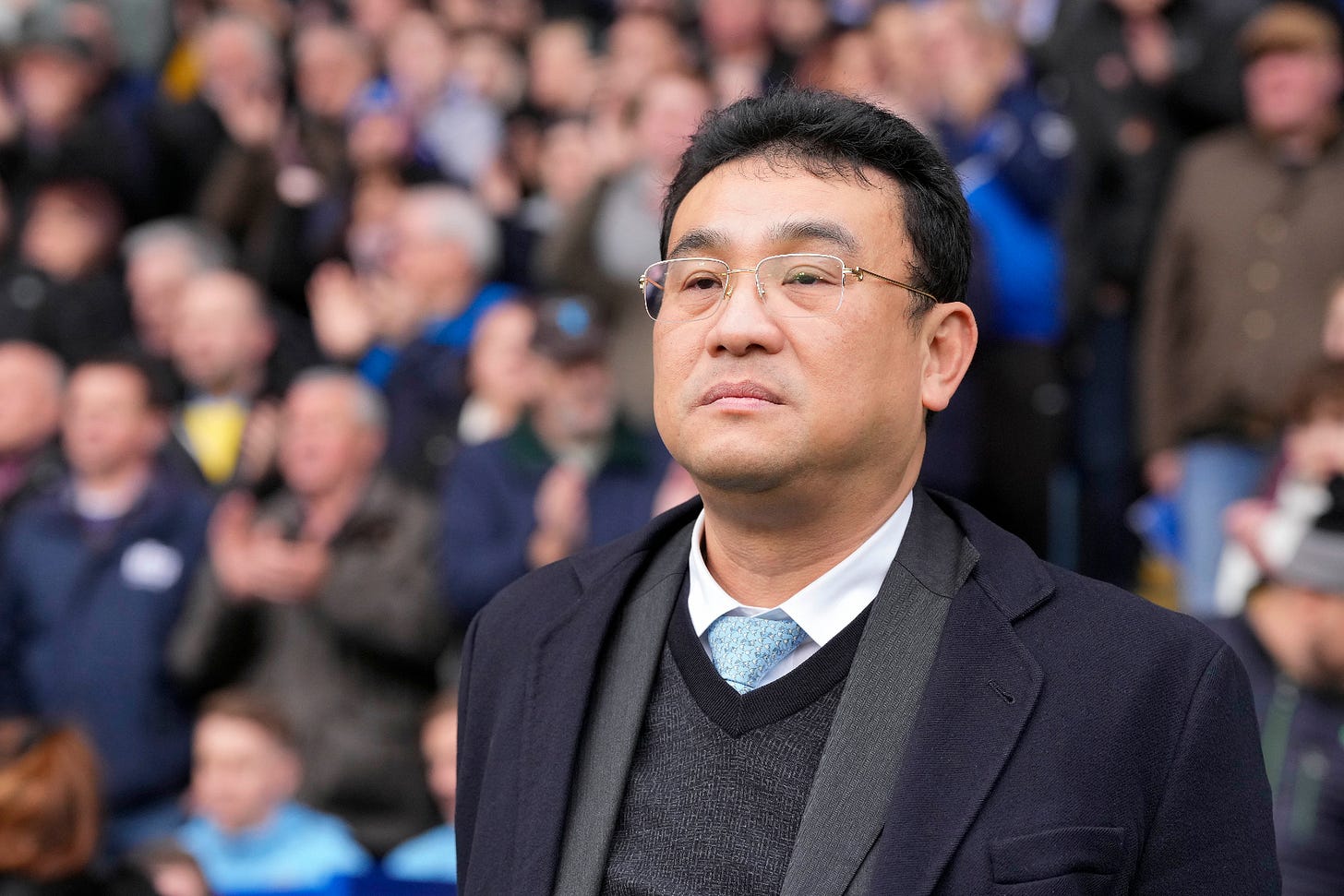 A portrait of Dejphon Chansiri standing in a suit in front of fans at Hillsborough