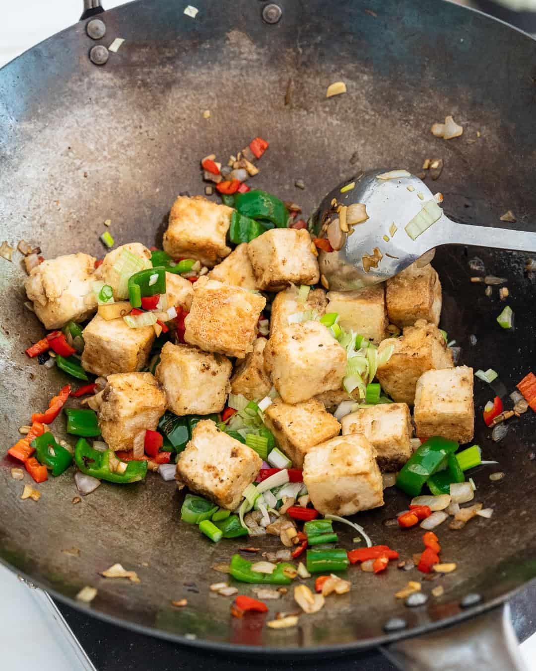 Adding the tofu and spring onions to the wok with the sautée veggies.