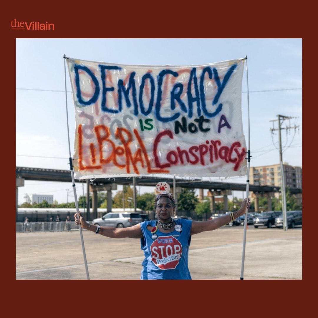 Person holds "Democracy is not a Liberal Conspiracy" sig outside the DNC.