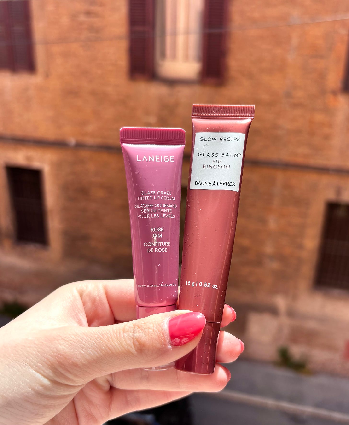 A side-by-side comparison of Laneige Glaze Craze Tinted Lip Serum in Rose Jam and Glow Recipe Glass Balm in Fig Bingsoo tubes being held in hand.