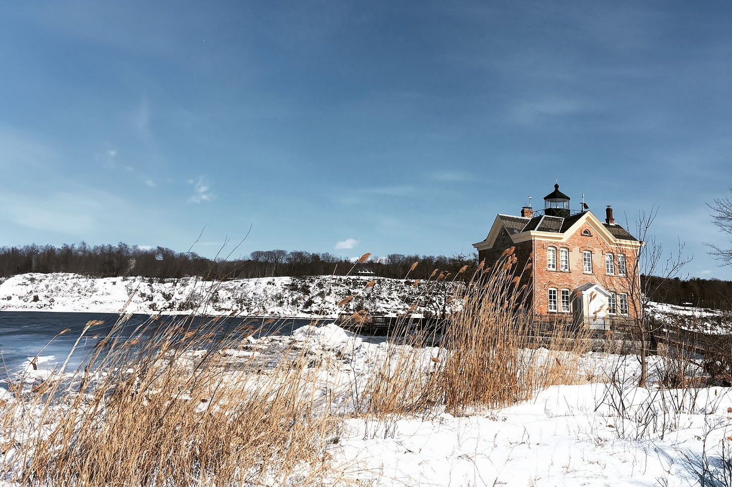 A lighthouse sits next to the Hudson River, surrounded by snow covering the ground.