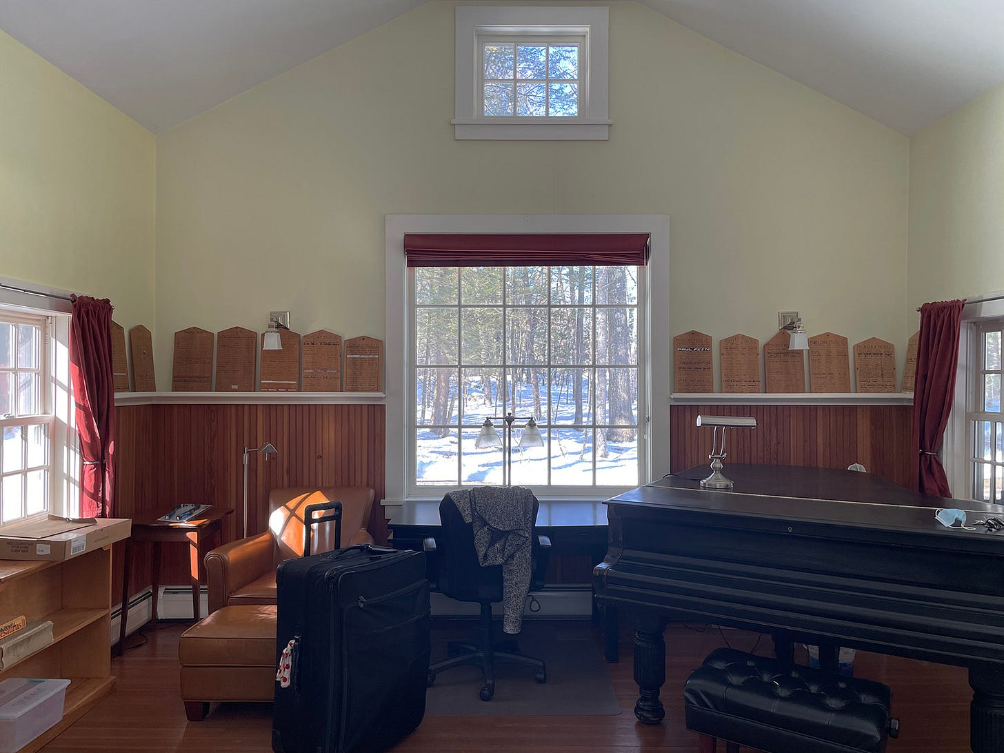 an artist studio with a piano, desk, and a large window with a view of trees and snow