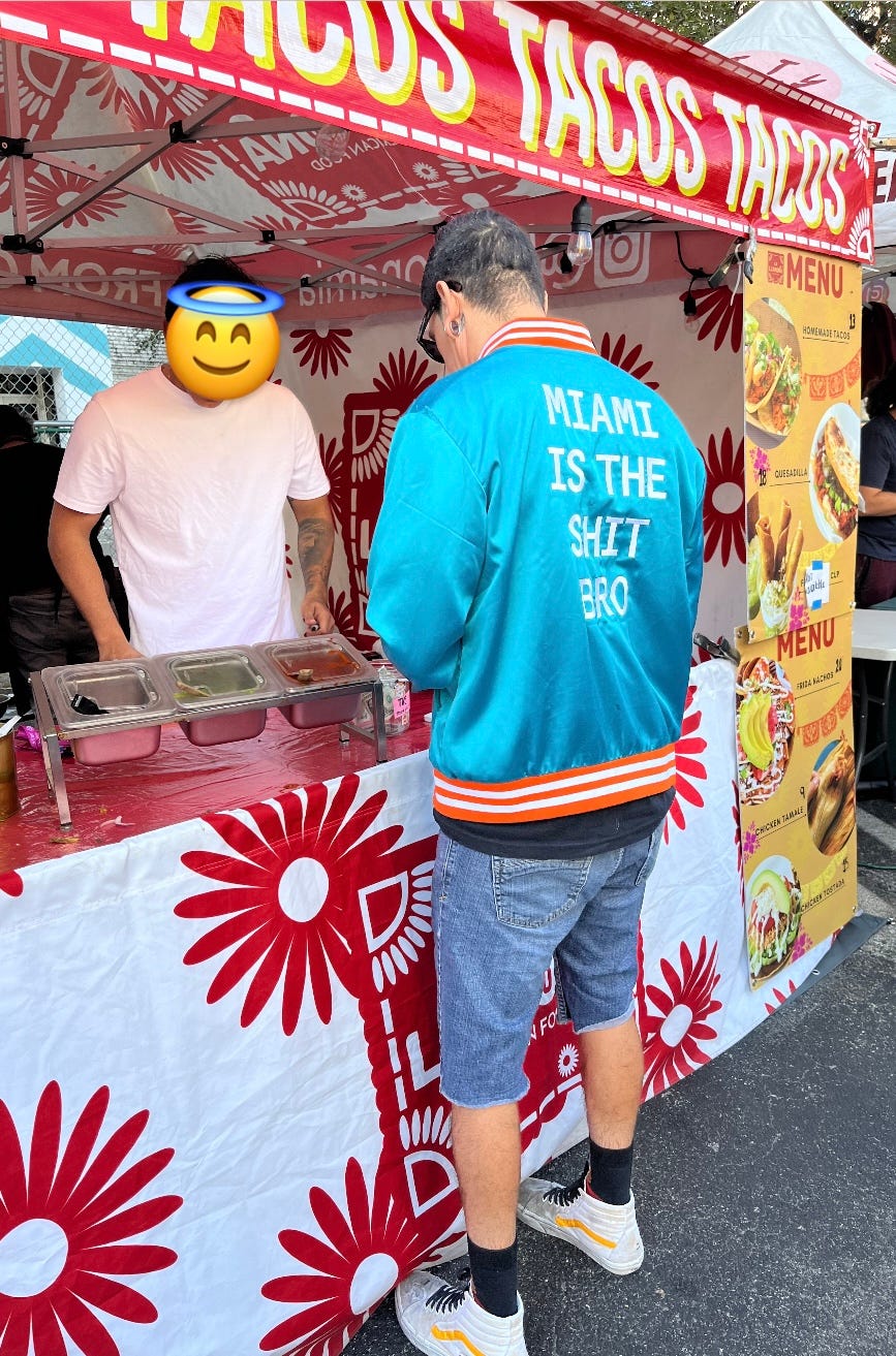 Photo of a man standing at a taco stand wearing a jacket in Miami Dolphins colors that says "MIAMI IS THE SHIT BRO" on the back Photo of a man standing at a taco stand wearing a jacket in Miami Dolphins colors that says "MIAMI IS THE SHIT BRO" on the back