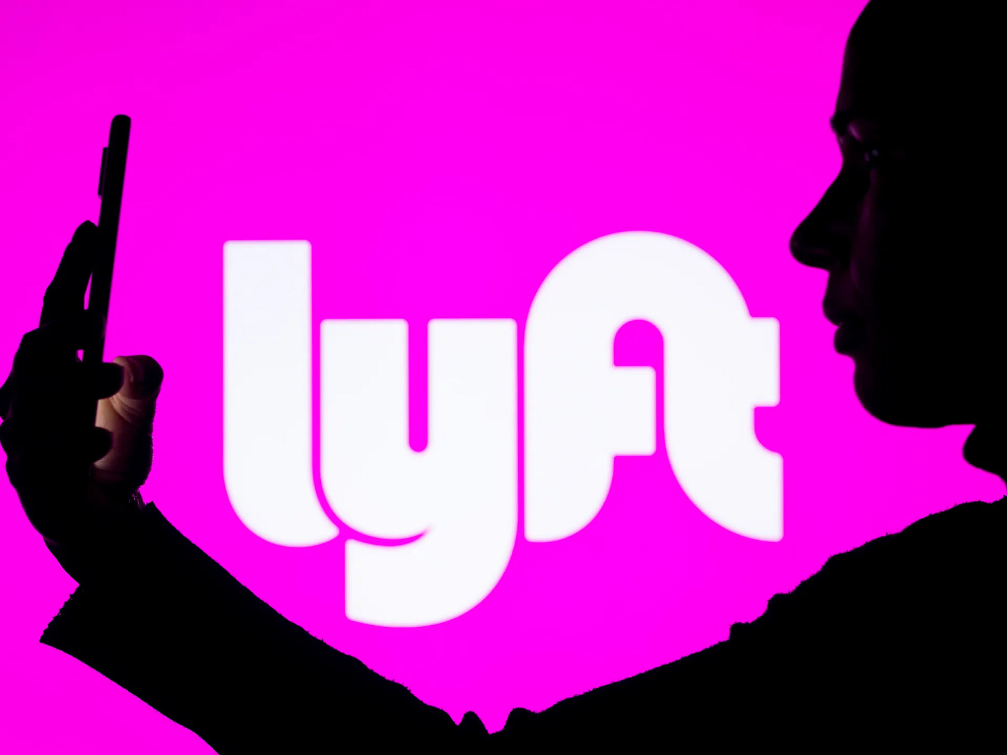 Shadow profile of a man holding a camera up to his face for a selfie against a hot pink backdrop with the Lyft logo in the middle. 