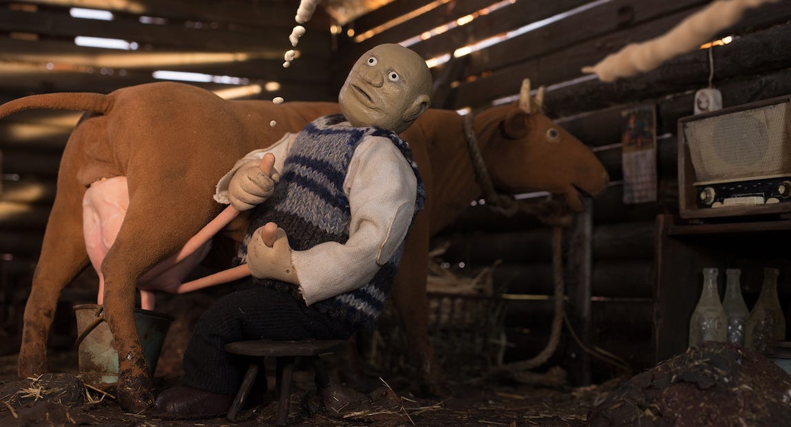 Claymation still of old man, eyes open disturbingly, wearing seater, holding two long rods attached to the udder of a cow. The scene is set in a milking shed. Claymation still of old man, eyes open disturbingly, wearing seater, holding two long rods attached to the udder of a cow. The scene is set in a milking shed.