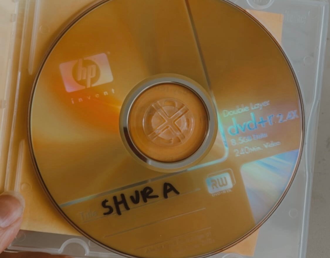 Photo of a gold re-writeable DVD-ROM in a clear case, with “Shura” written in black permanent marker 