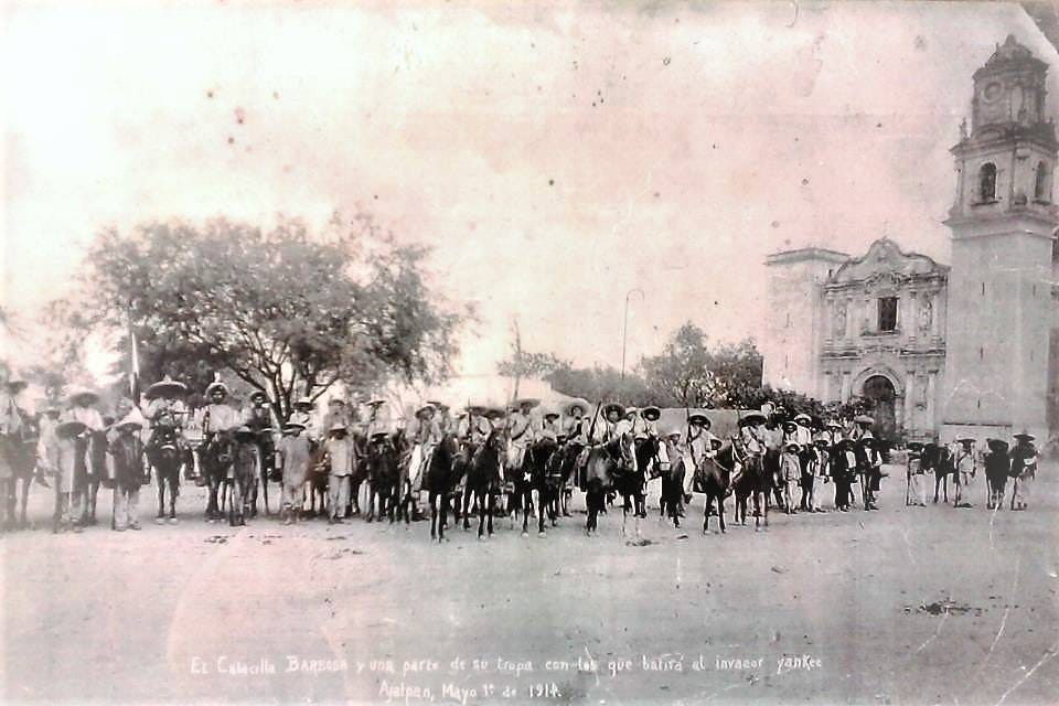 Fotografía en blanco y negro en que aparece un grupo de revolucionarios al mando del General Francisco Barbosa J. frente a la Iglesia de Coculco. Texto en la imagen: El Cabecilla Barbosa y una parte de su tropa con los que batirá al invasor Yankee. Ajalpan, Mayo 1o. de 1914.