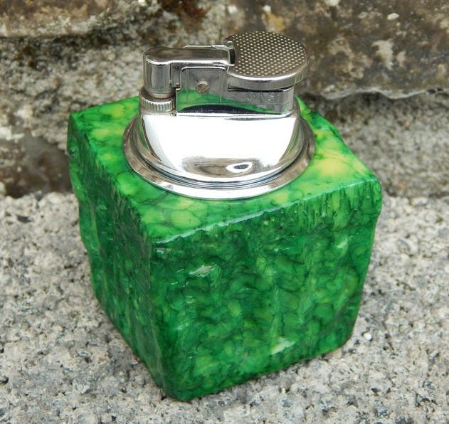May include: A green and white lighter with a chrome top. The lighter is made of a textured material that resembles stone.