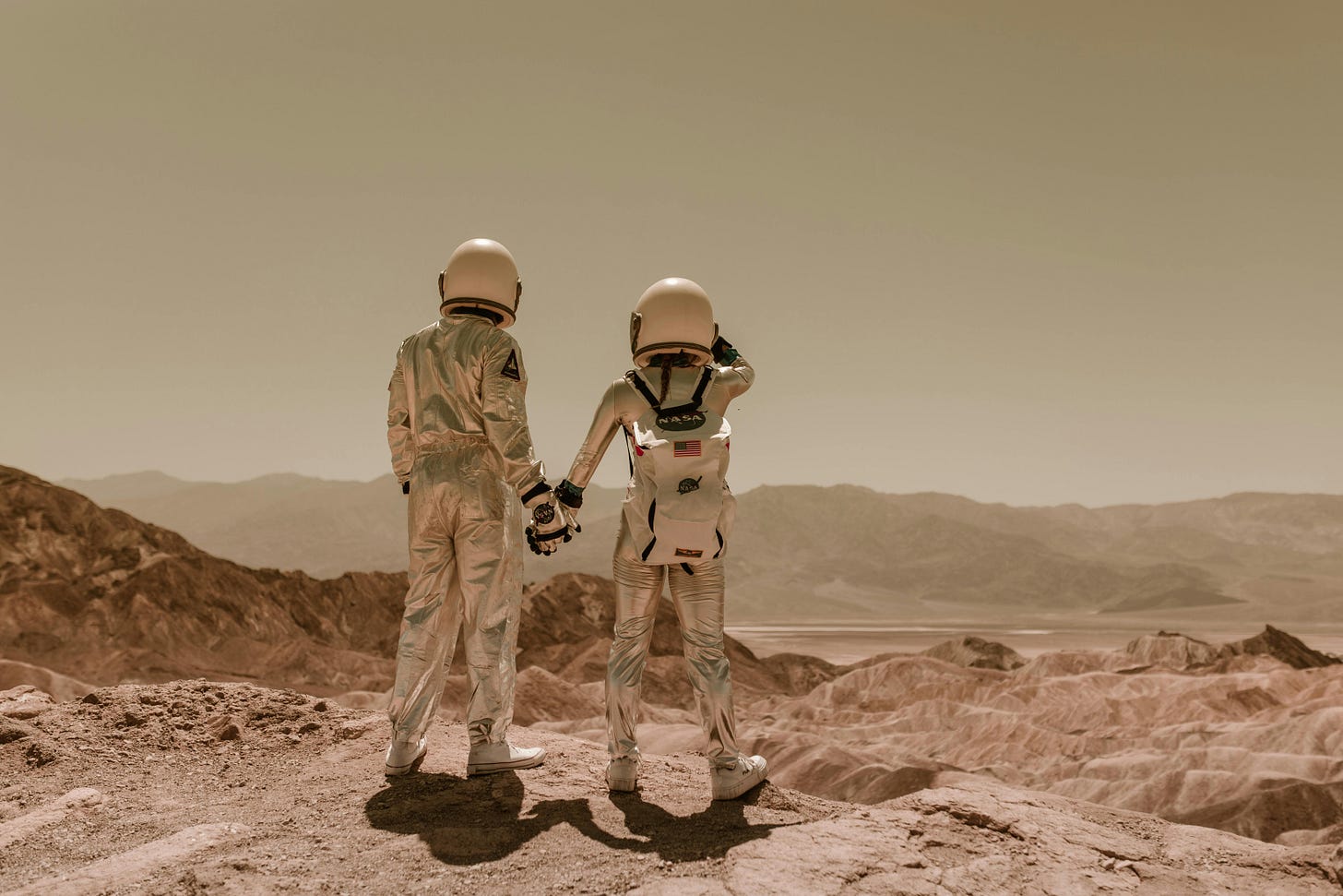 two astronauts holding hands on rocky desert landscape