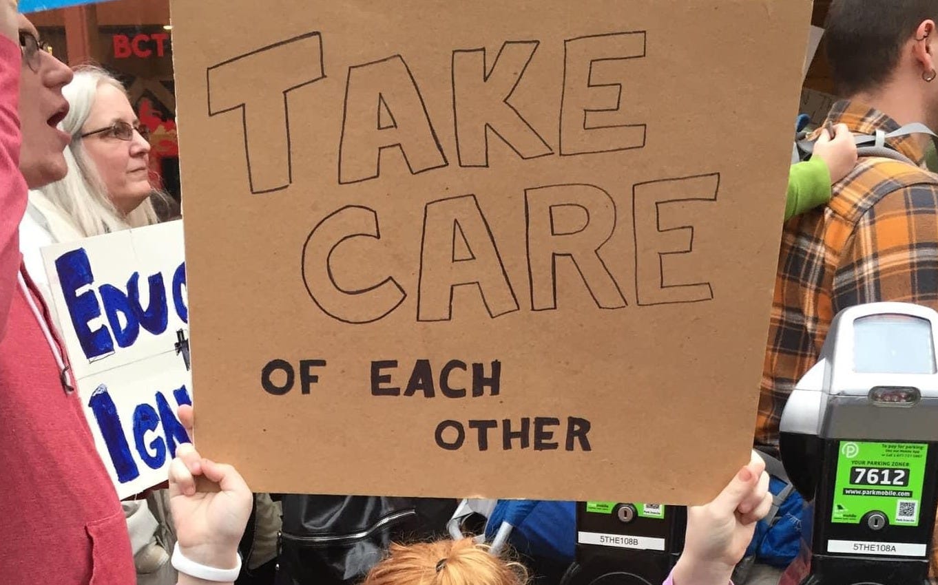 Photo of a cardboard protest sign held by a child reading 'Take Care of each other'