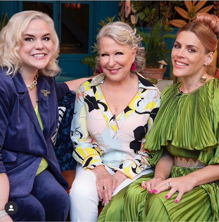 Busy, Caissie and Bette Midler are posing on the set of Busy This Week. Busy is wearing a pleated olive green evening gown. Caissie is wearing a navy velour suit with a lime green shell under the jacket. Bette is wearing a Pucci top in white, blue, black and yellow with white pants. In one photo, they sit smiling. In one photo Busy is posing playfully with her back to the camera. In another, Caissie poses alone to show off her suit. In the final photo, the trio are at the murphy bar on set and they are sharing a huge laugh.