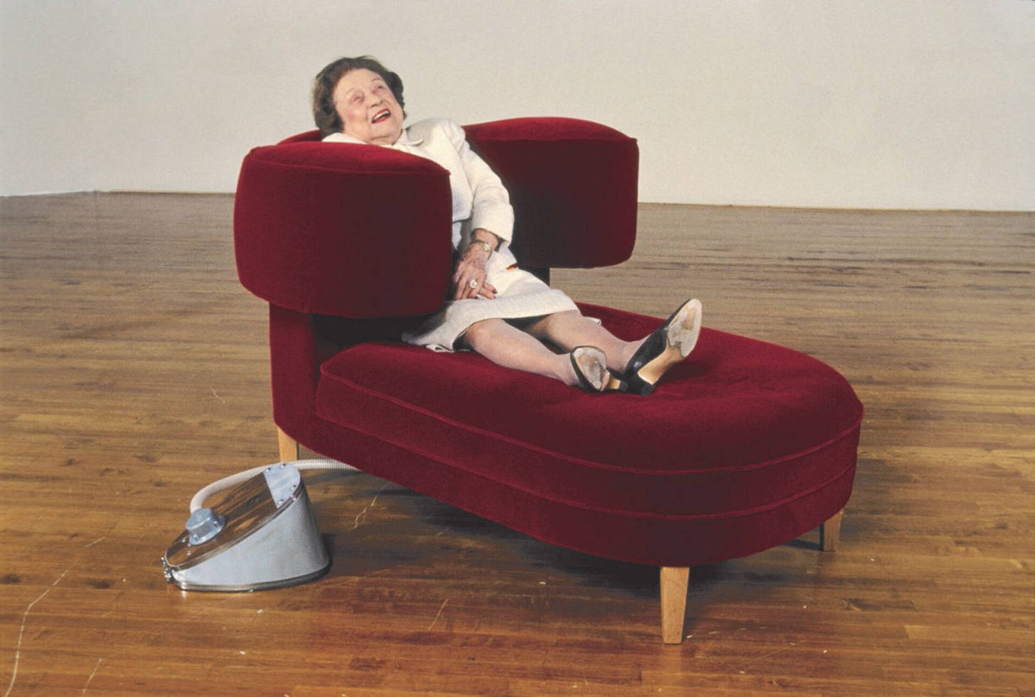 A woman reclining in a large enveloping red lounger in a gallery space.