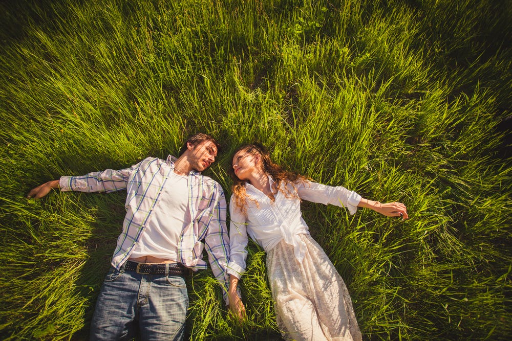 Man and woman lying in grass holding hands