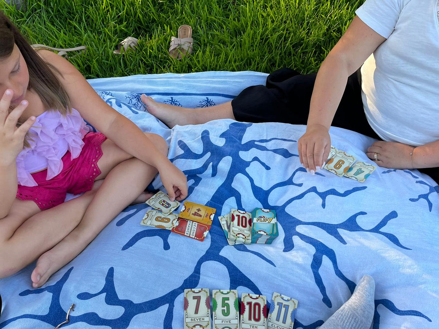 My wife and daughter playing a card game on a towel on the grass of a public green area near our hometown
