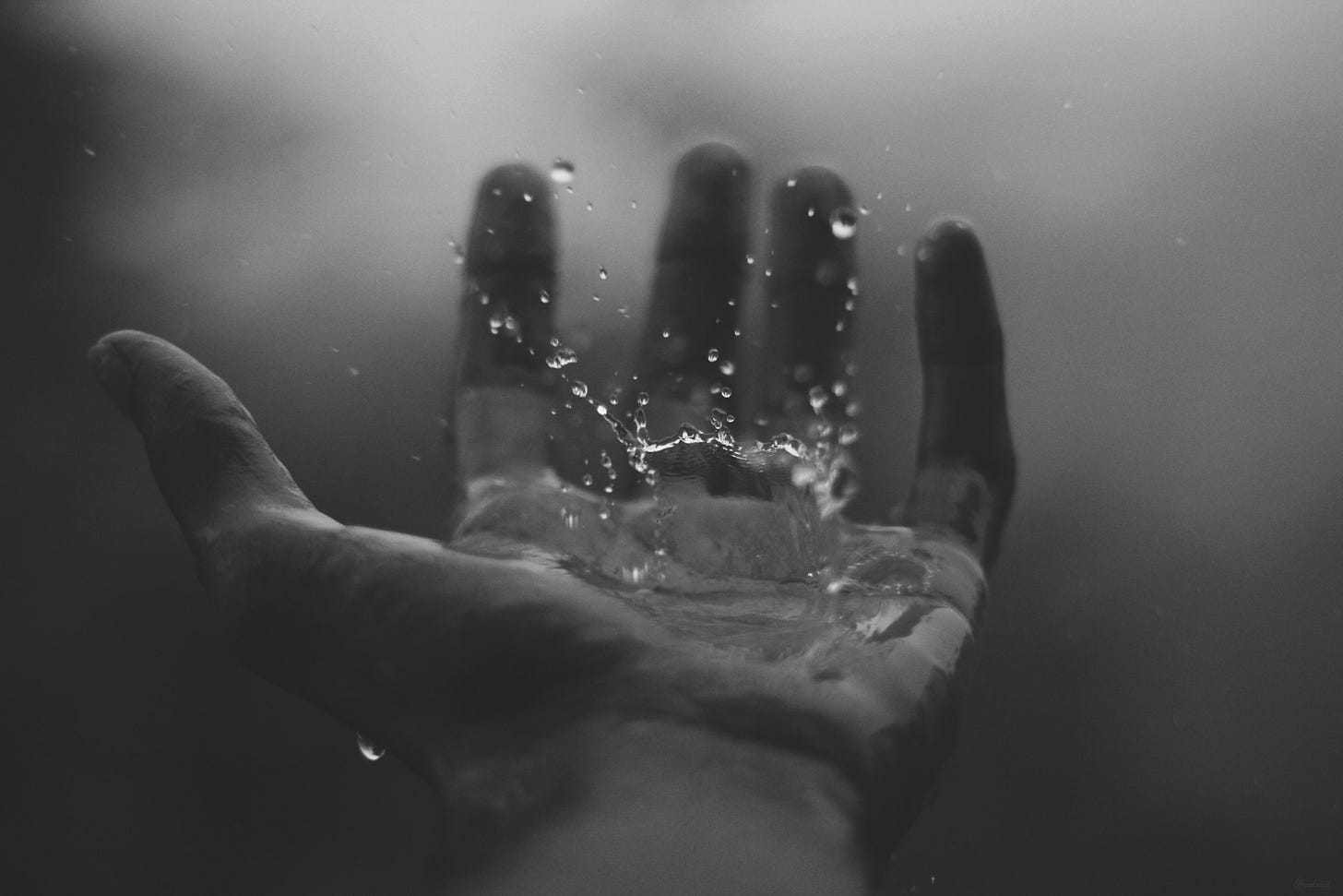 A raindrop splashes in someone's left hand. The picture is black and white. A raindrop splashes in someone's left hand. The picture is black and white.