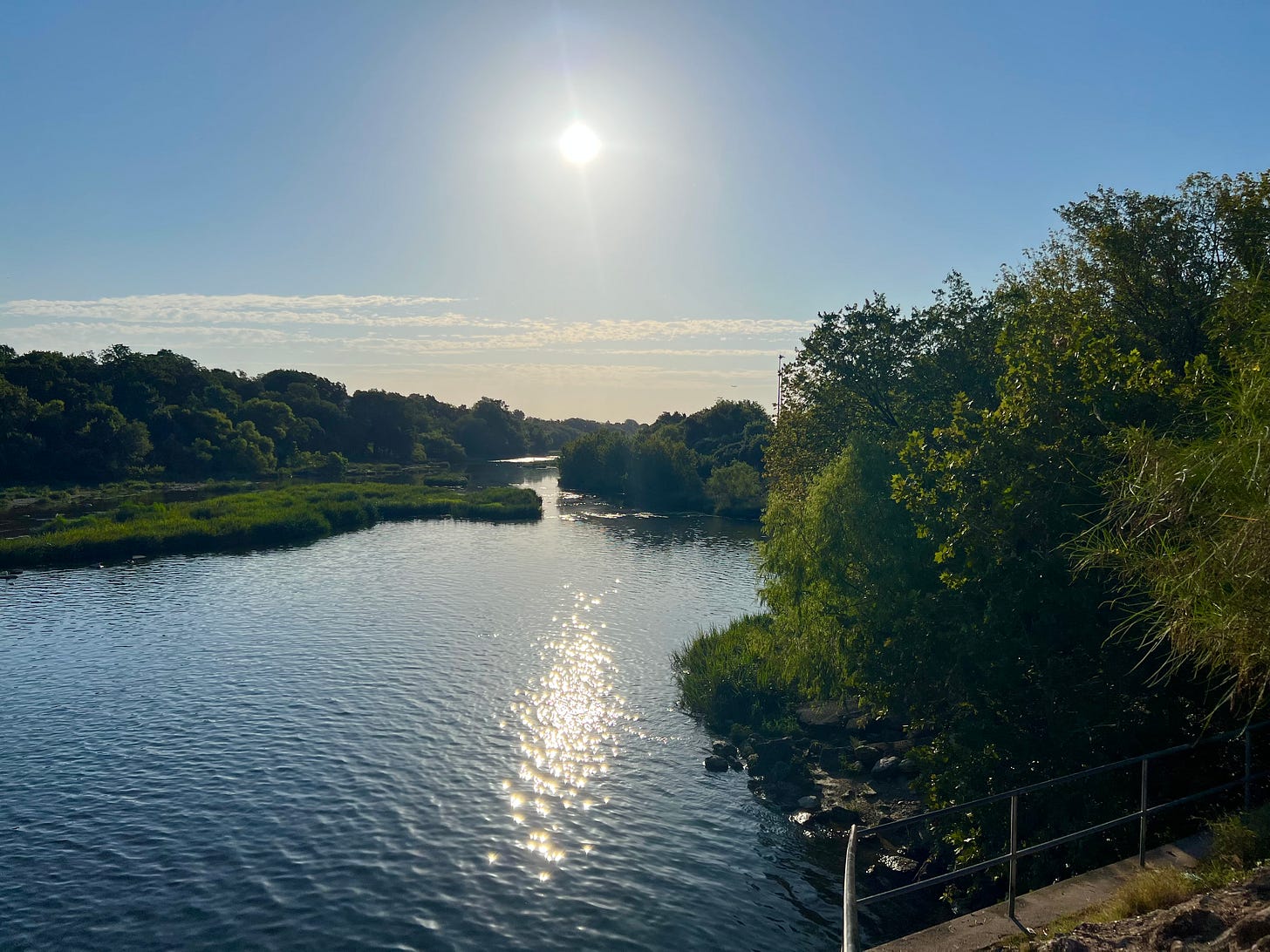 View of urban river with green forested banks and rising sun