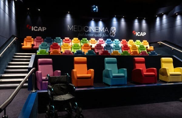 A cinema with rose of chairs in bright colors, and the words “MediCinema, feel better with film” on the back wall.