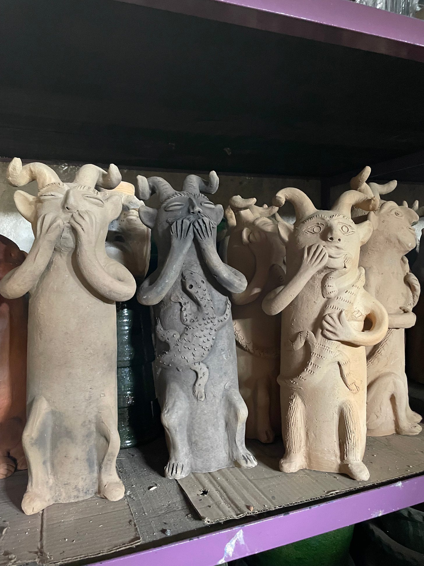 Three clay statues of demons covering their mouths as if they've been surprised by something.