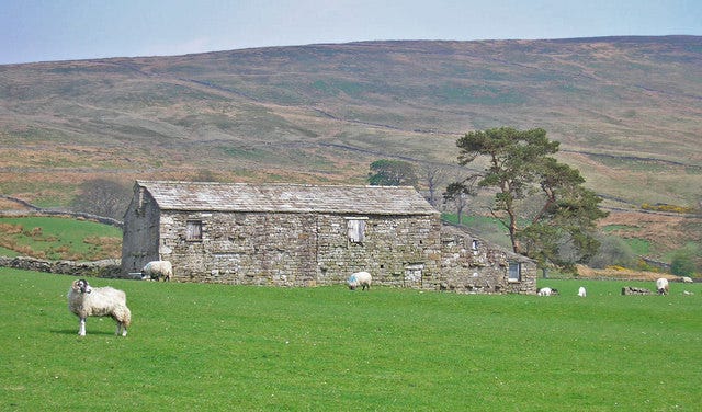 A stone barn in a green valley, with hills sloping up behind it under an open sky.