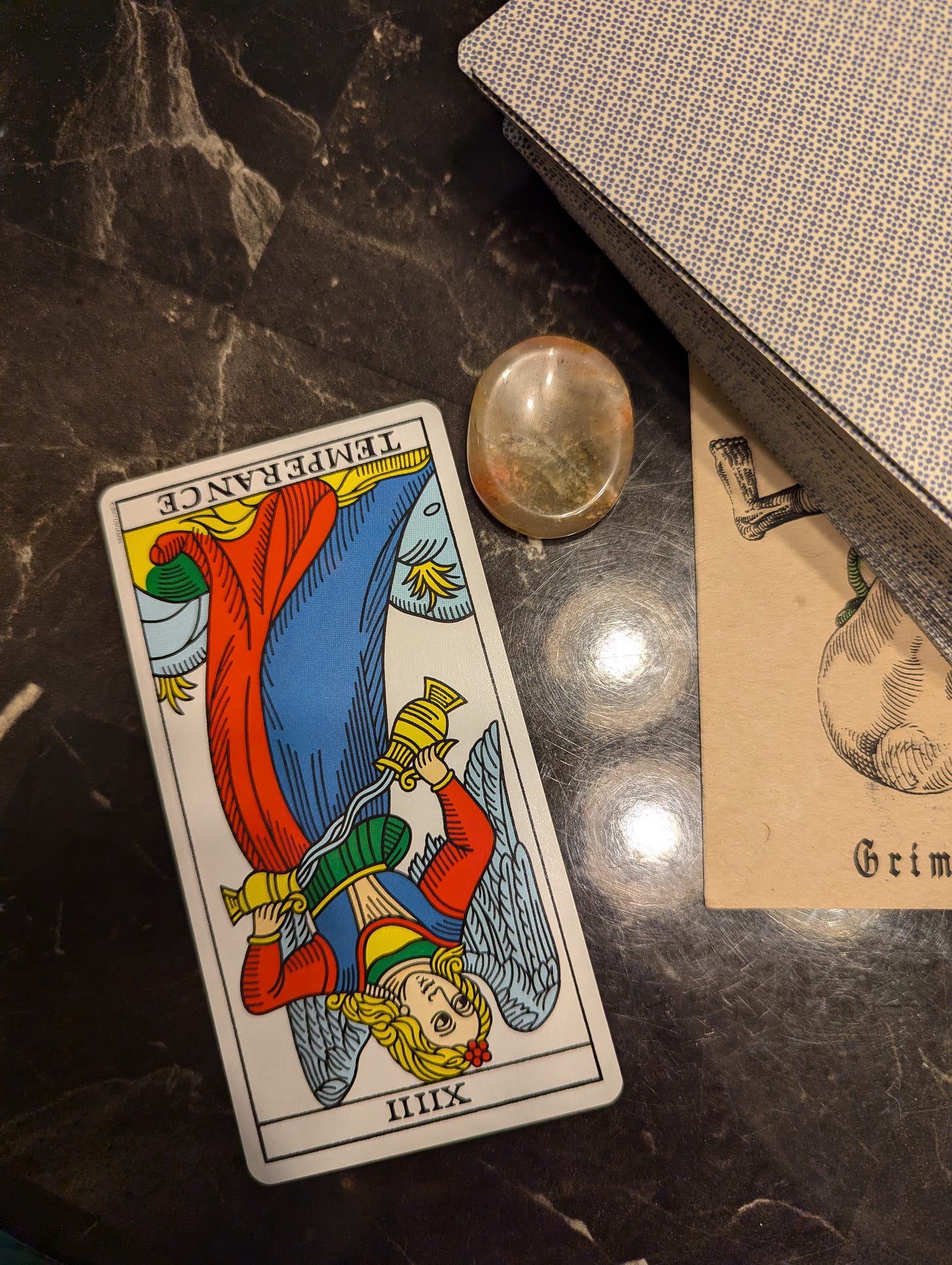 Temperance reversed next to a worrying stone and a stack of cards on a faux marble table.