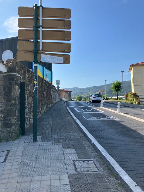 a roadside yellow arrow marking path, the soda machine on route, a view of descent into Bilbao