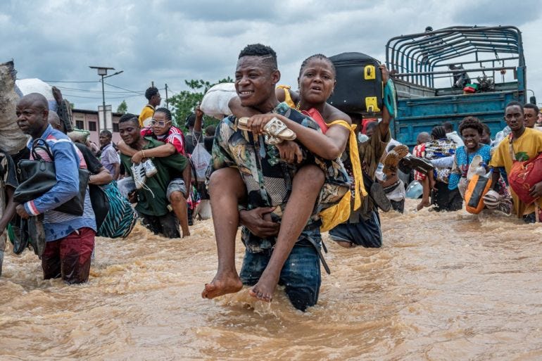 A resident carries a woman as others wade through floodwaters in the Ndjili district of Kinshasa on April 6, 2025. [Hardy Bope/AFP]