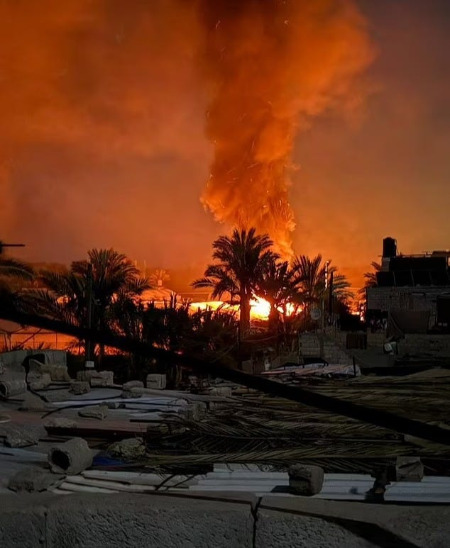 Large fire burning behind palm trees at night.