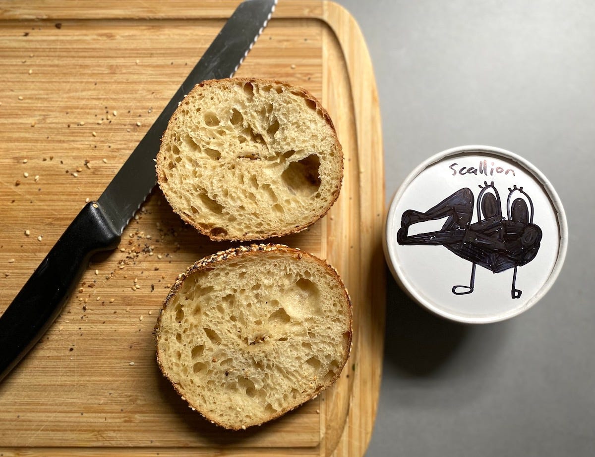 A sliced everything bagel and tub of cream cheese.
